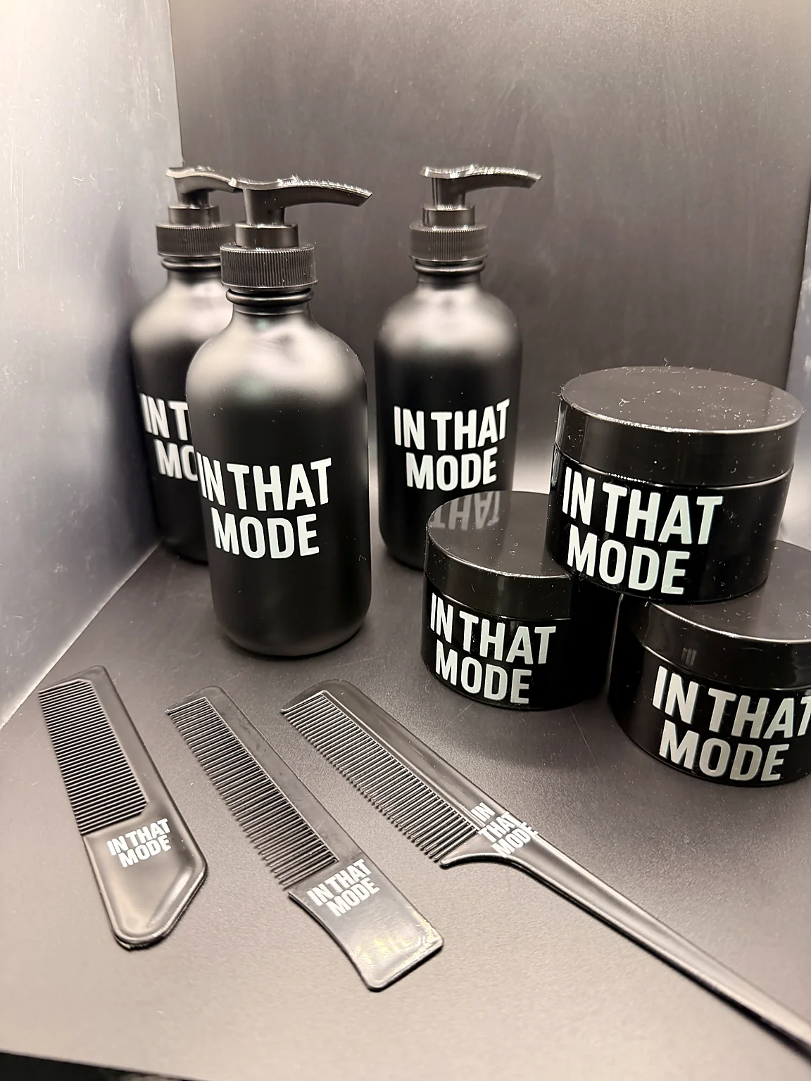Black grooming bottles, containers, and combs branded In That Mode